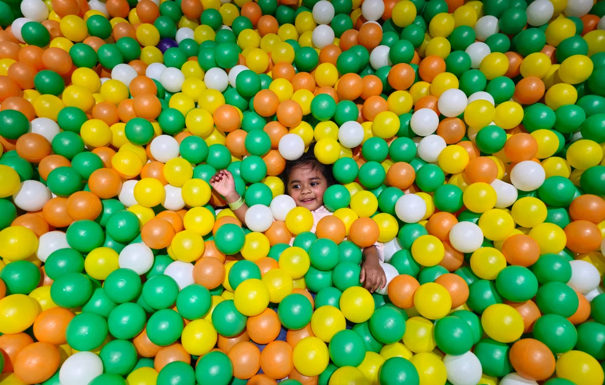 A toddler laughing in a ball pit filled with green, yellow and orange balls